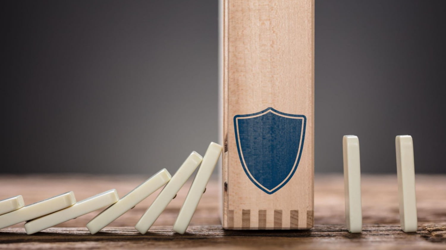 Ein hölzerner Block mit Schild-Symbol hält fallende Dominosteine auf