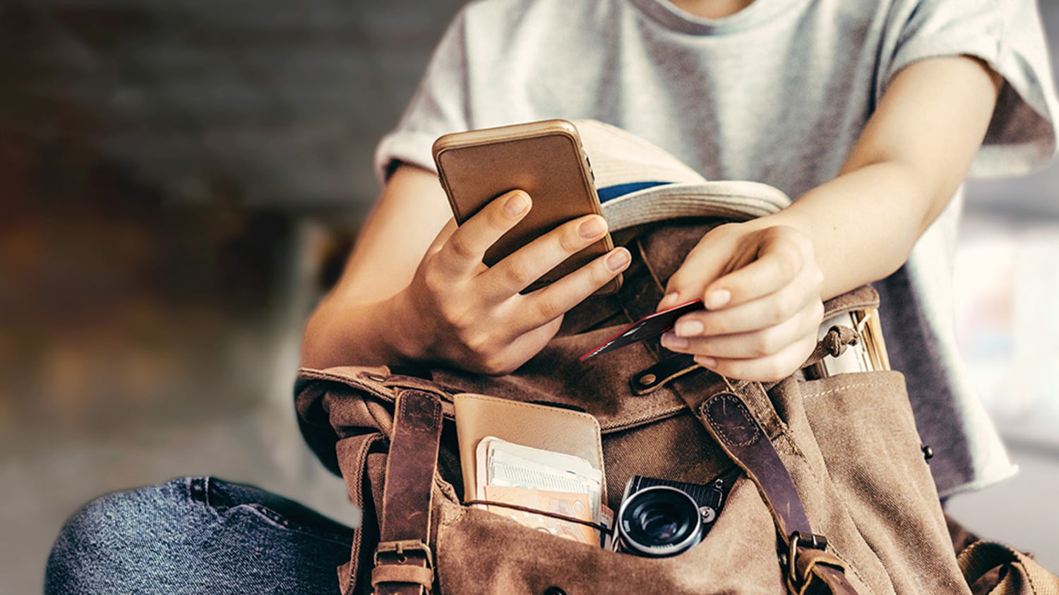 Junger Mann nimmt sein Handy und die Kreditkarte aus dem offenen Rucksack