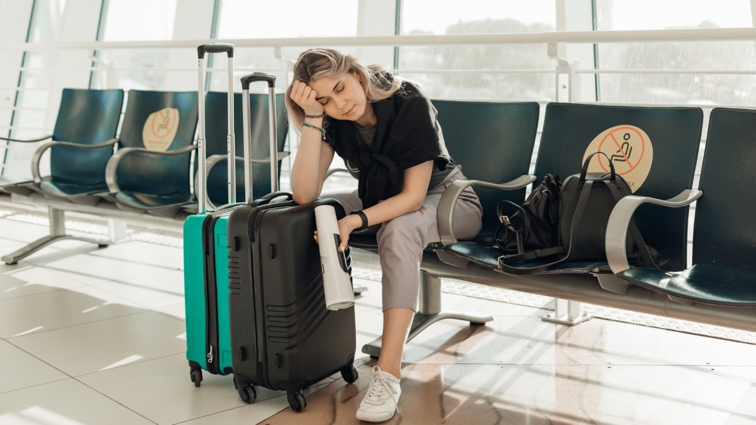 Eine junge Frau sitzt mit ihrem Gepäck niedergeschlagen in einer Wartehalle im Flughafen