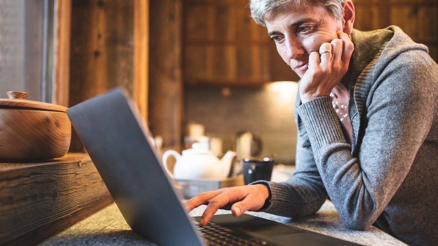 Eine Frau betrachtet in ihrer Küche skeptisch den Bildschirminhalt ihres Laptops