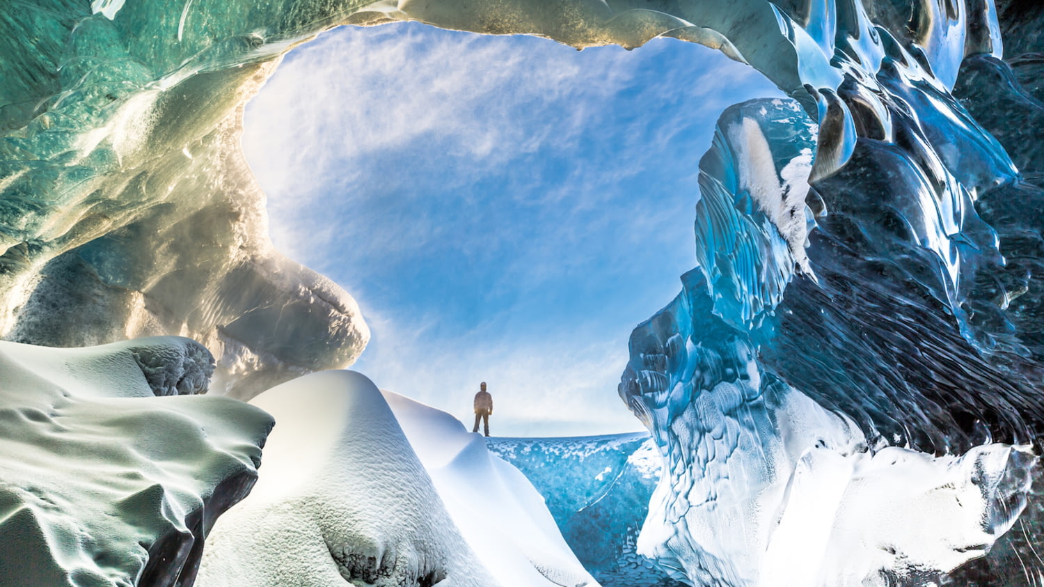 Person steht vor dem Eingang einer riesigen Gletscherhöhle