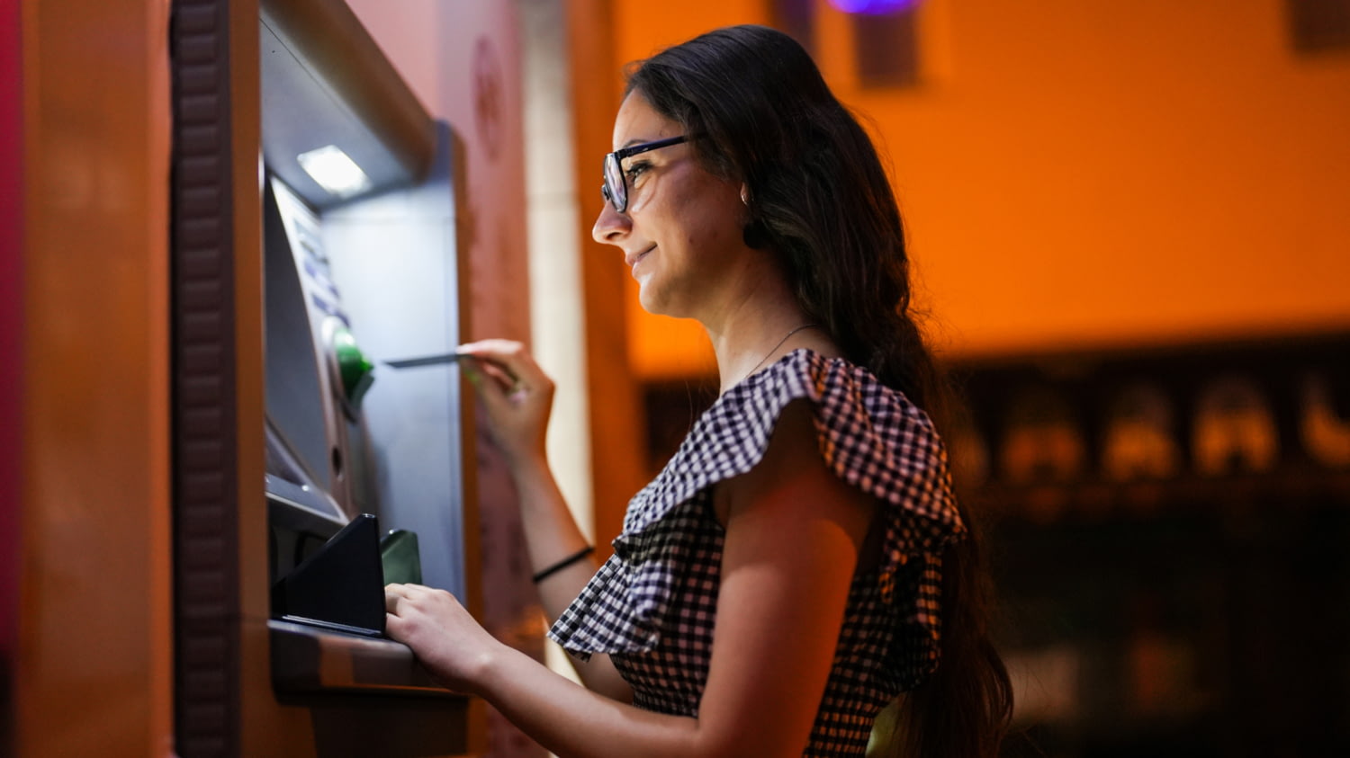 In einer Straße führt eine Frau abends eine Karte in einen Geldautomaten ein