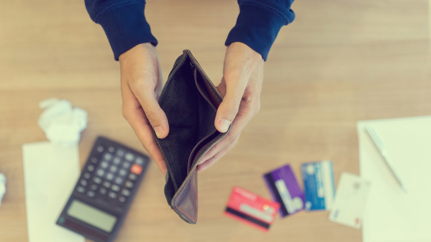 Ein Mann hält eine leere Börse und auf dem Boden liegen Rechnunge, Kreditkarten und ein Taschenrechner