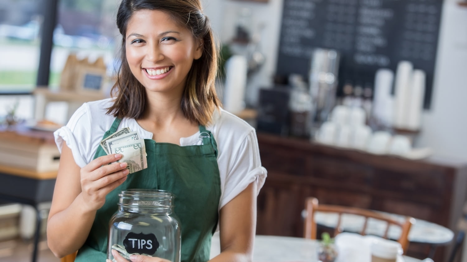 Eine Kellnerin steckt ihr Trinkgeld in ein Sammelglas