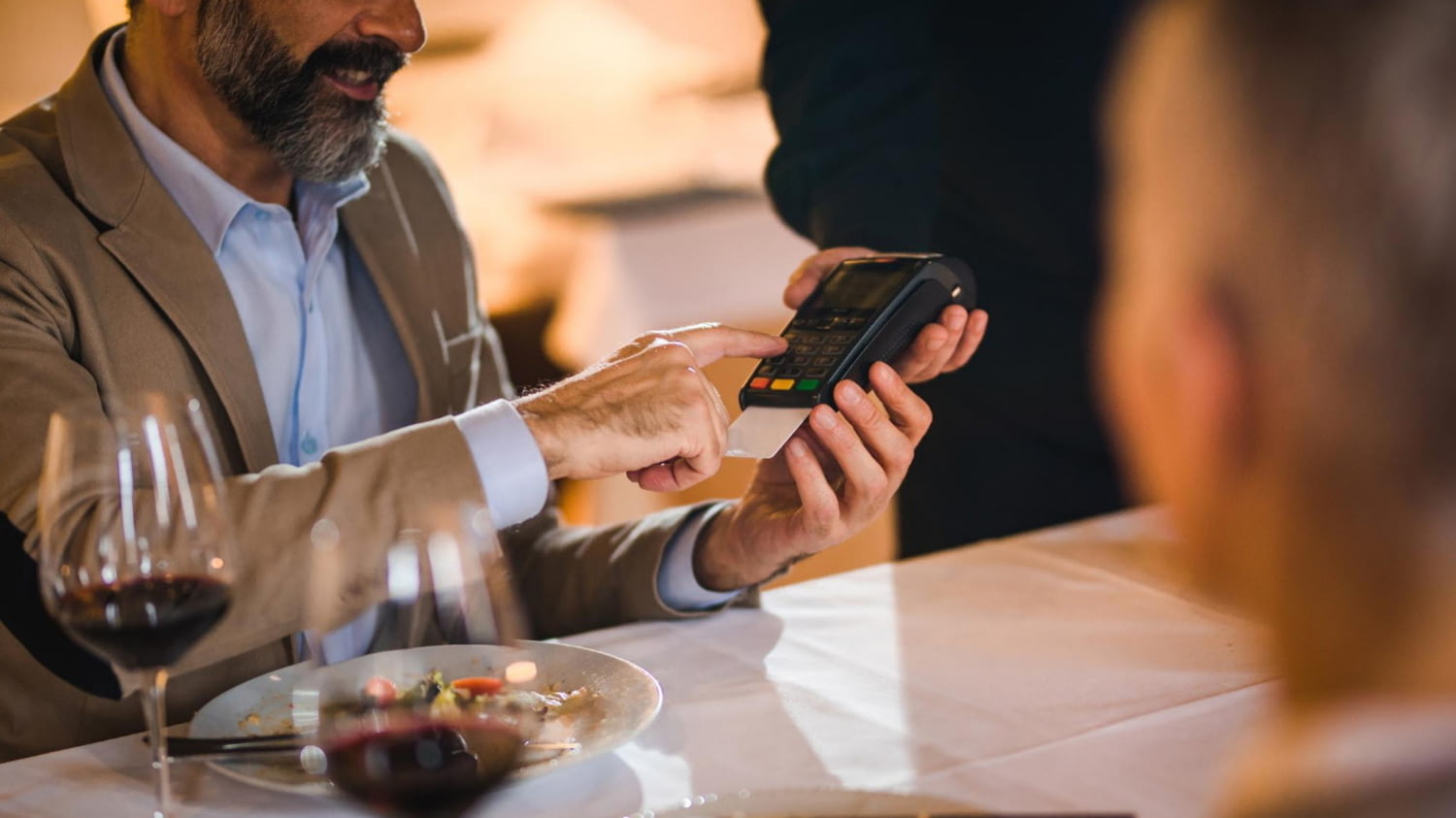 Mann bezahlt in einem Restaurant mit Kreditkarte und gibt dazu seine PIN ein