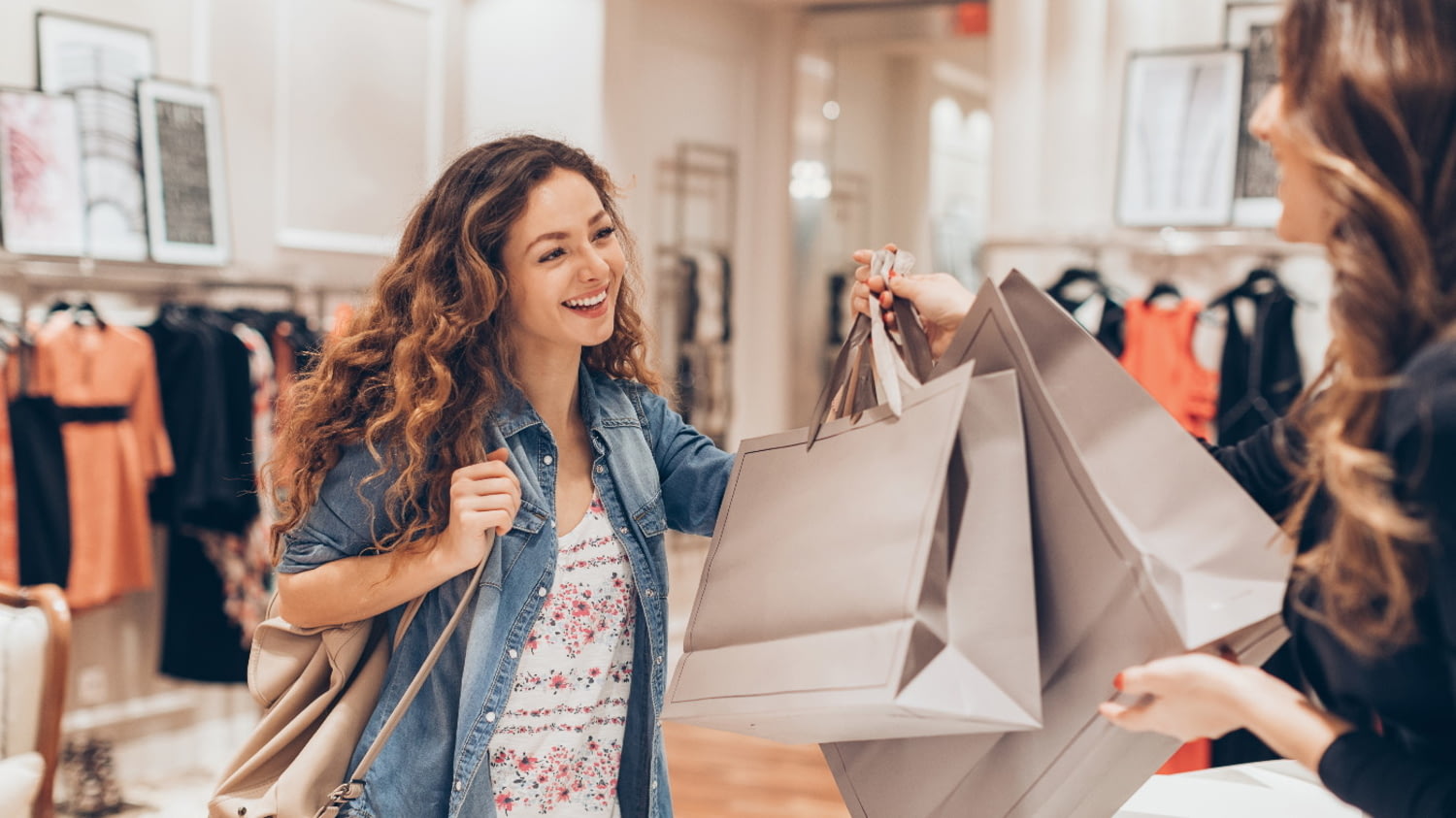 Eine junge Frau nimmt zwei Taschen mit Einkäufen an der Kasse einer Boutique entgegen