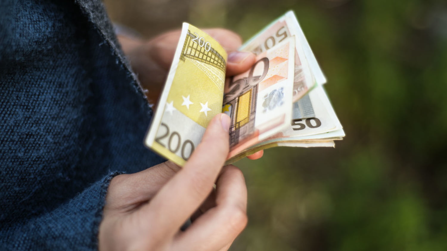 Person zählt Geldbetrag in größeren Euro-Banknoten.