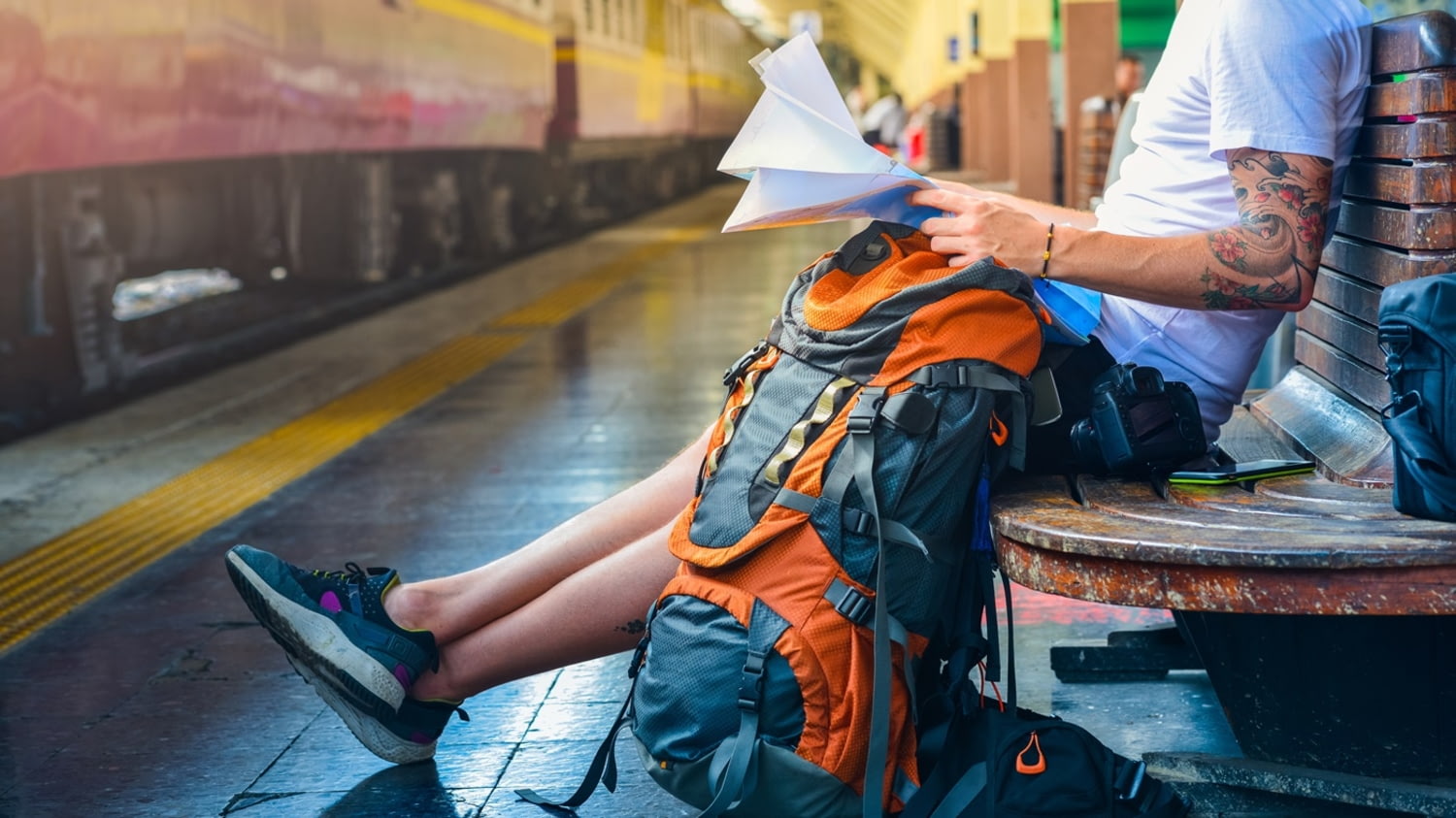 Ein Mann sitzt mit einem großen Rucksack auf einer Bank an einem Bahngleis.