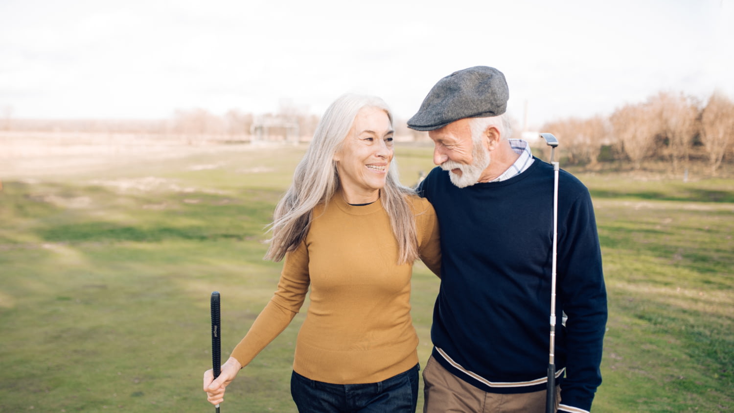 Ein älteres Ehepaar läuft auf dem Golfplatz Arm in Arm über den Rasen