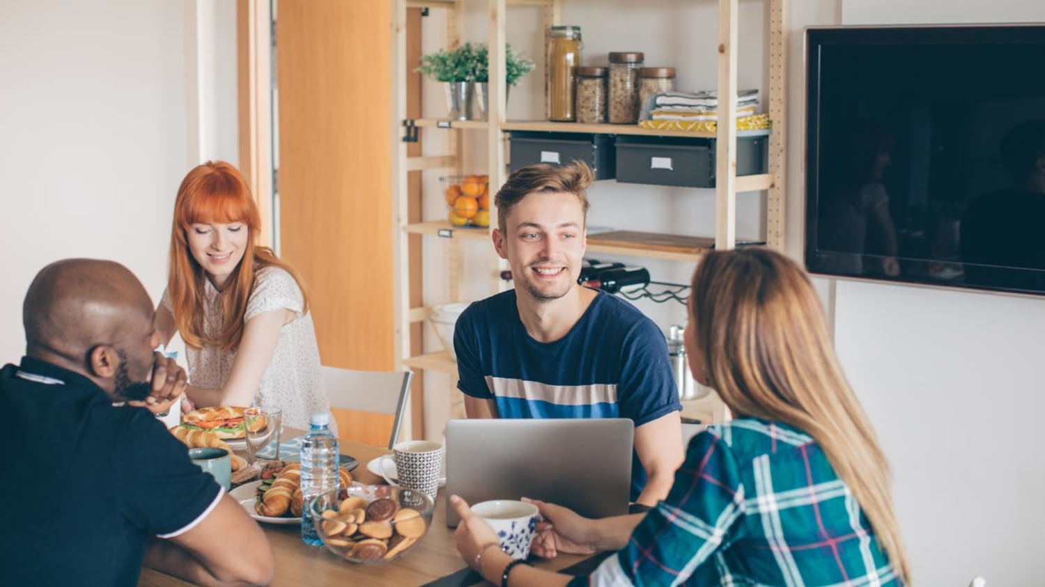 Vier junge Menschen frühstücken miteinander in einer Wohnung