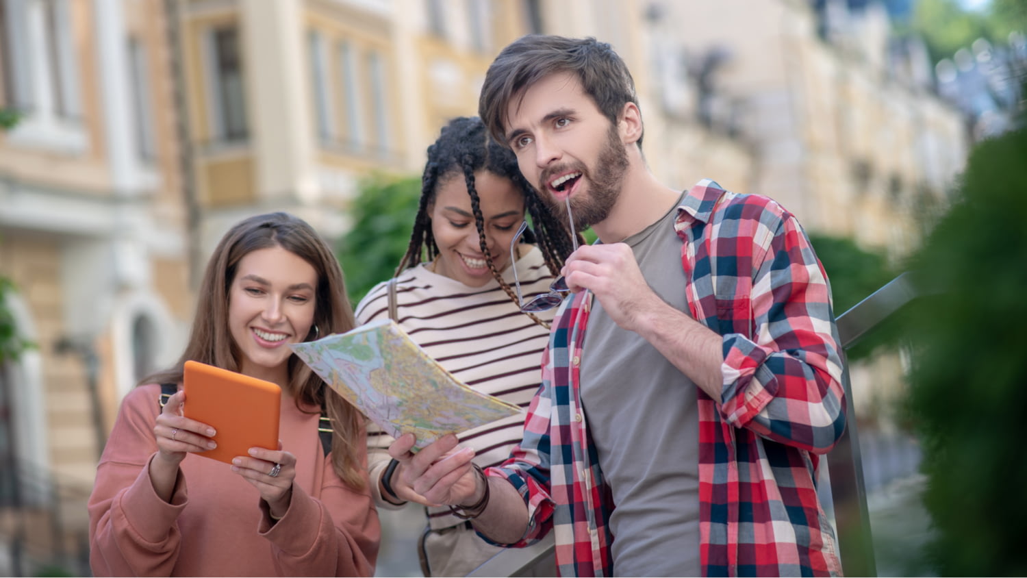 Drei junge Leute stehen mit Tablet und Landkarte in der Stadt