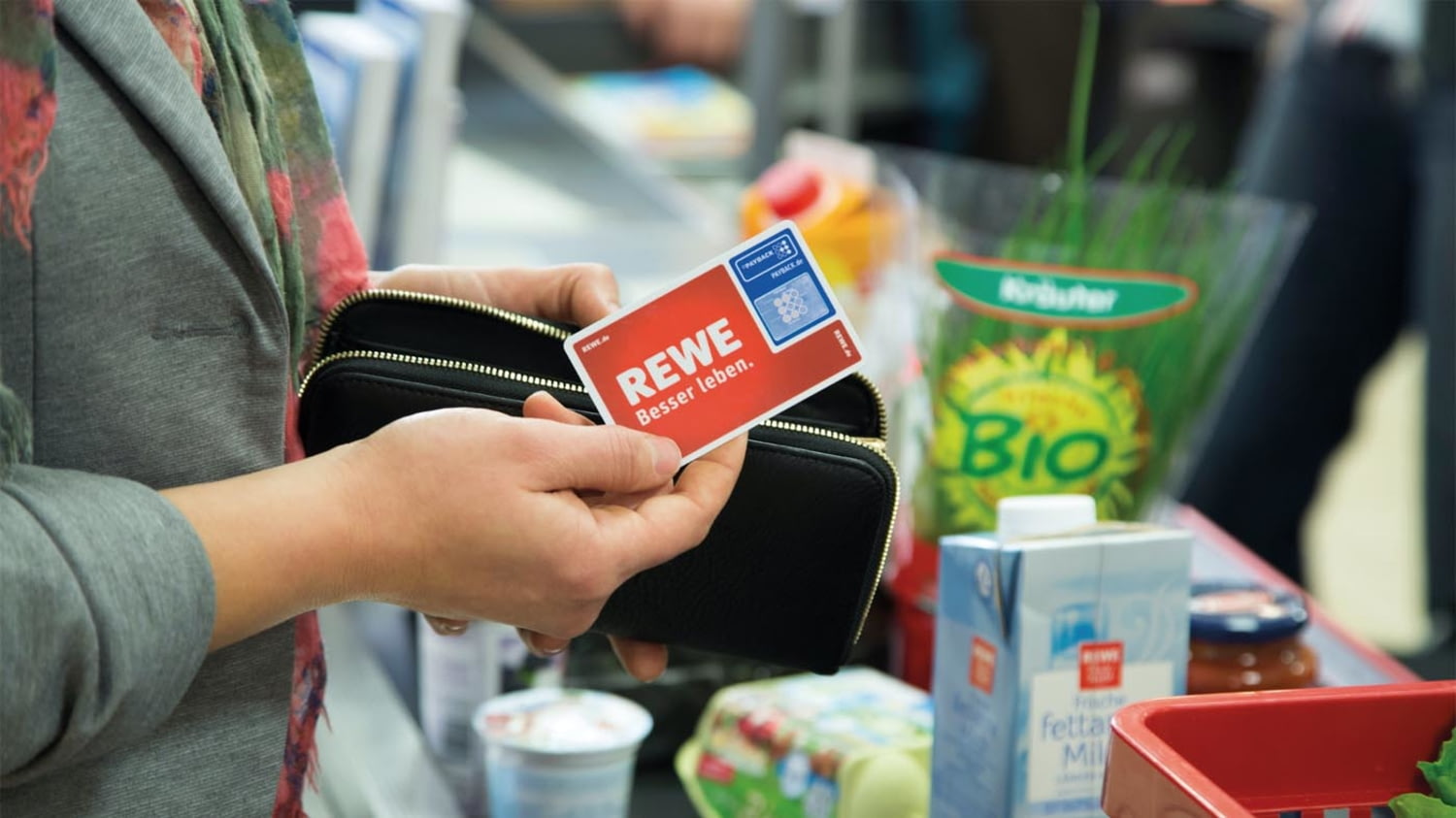 Eine Kundin hält an einer Supermarktkasse eine Paybackkarte von Rewe bereit