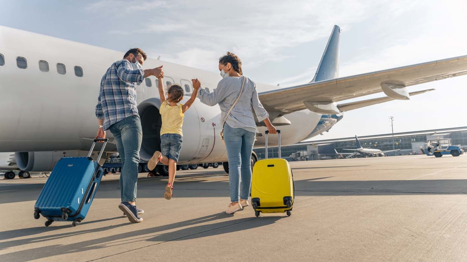 Eine junge Familie läuft mit ihren Koffern über das Rollfeld zum Flugzeug