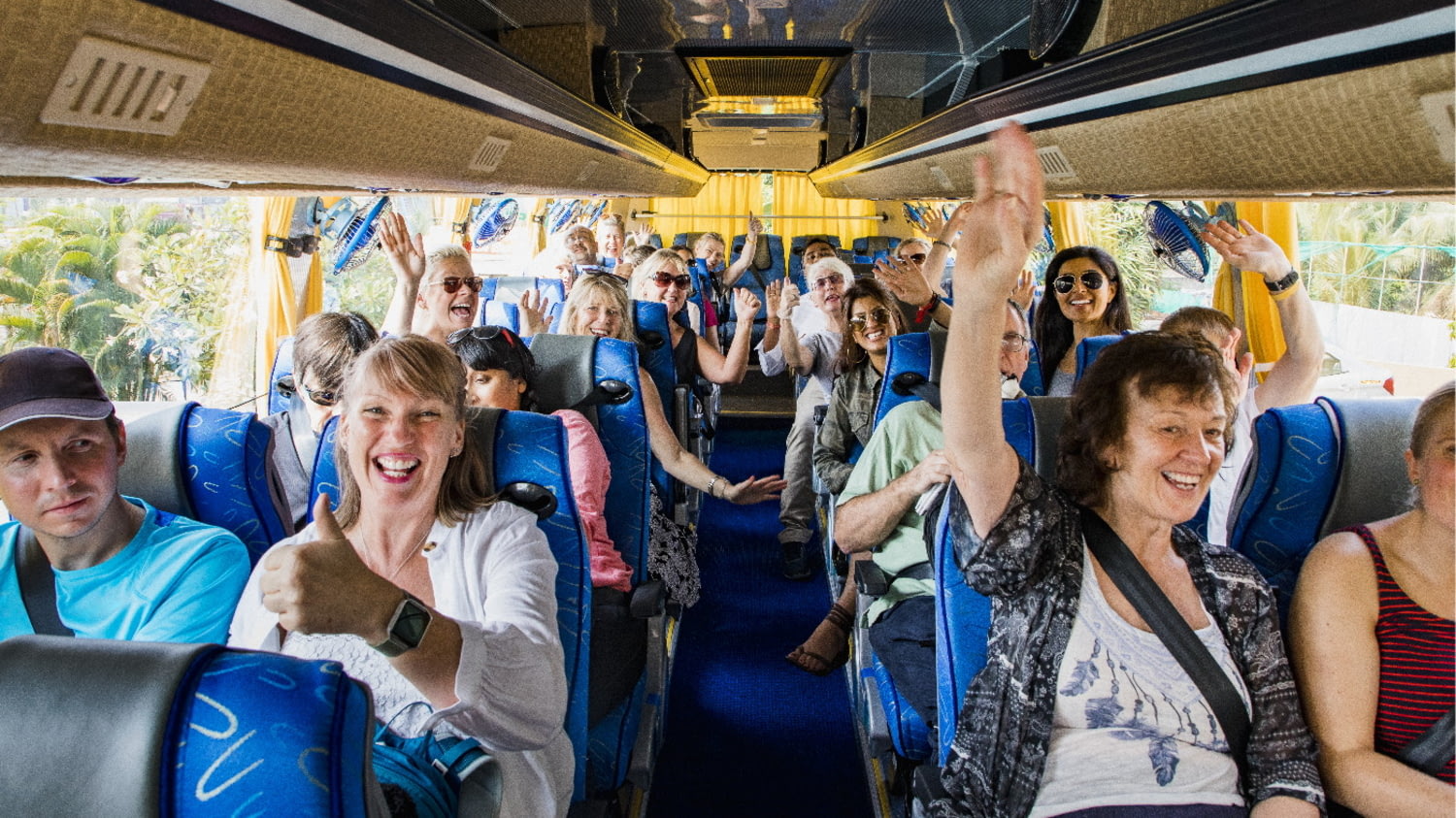 Eine Gruppe Urlauber sitzt gut gelaunt im Reisebus