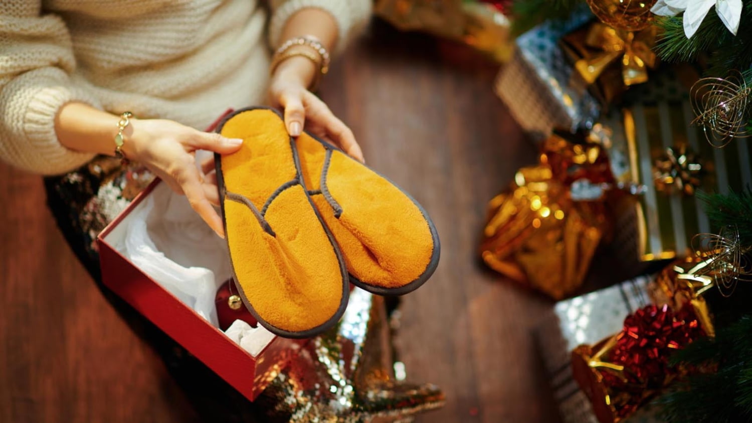 Elegant gekleidete Frau fördert beim Auspacken ihres Weihnachtsgeschenks ein Paar merkwürdige Hausschuhe zutage