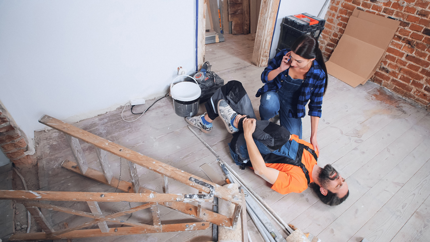 Handwerker liegt unter einer umgestürzten Leiter am Boden und hält sich das verletzte Bein