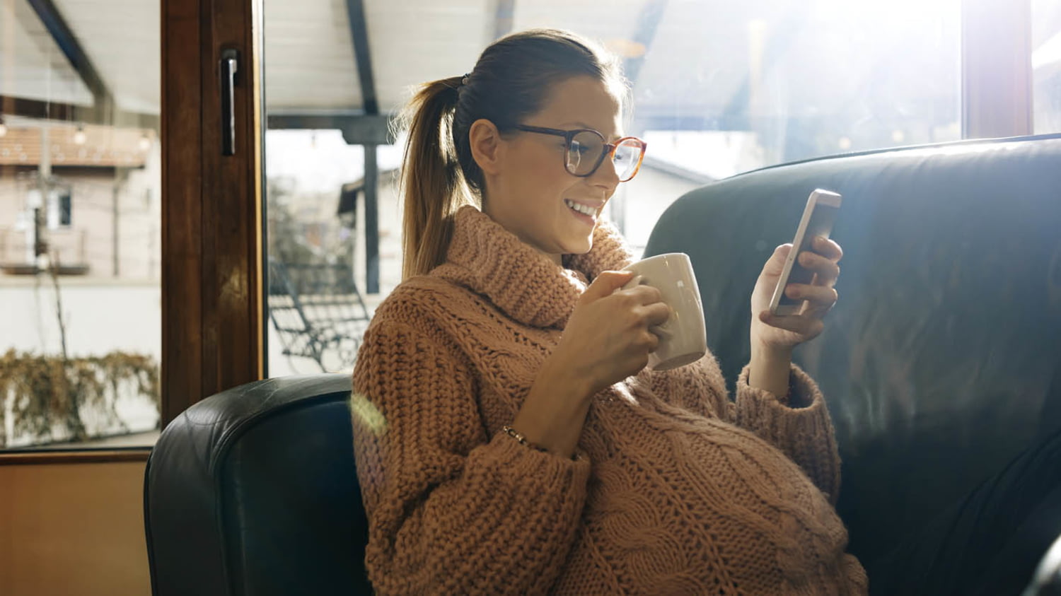 Entspannte Hochschwangere mit Kaffeetasse und Smartphone auf dem Sofa