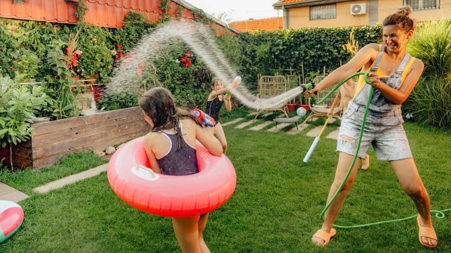 Junge Mutter spritzt Tochter mit Gartenschlauch nass