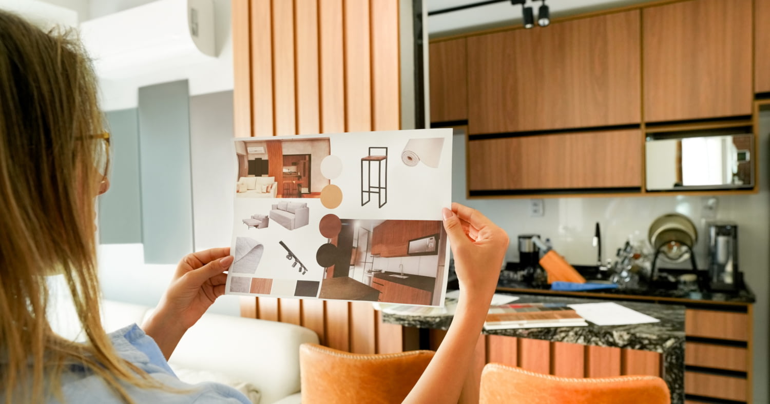 Eine Frau hält ein Blatt mit Inspirationsbildern für die Küche vor ihre aktuelle Küche