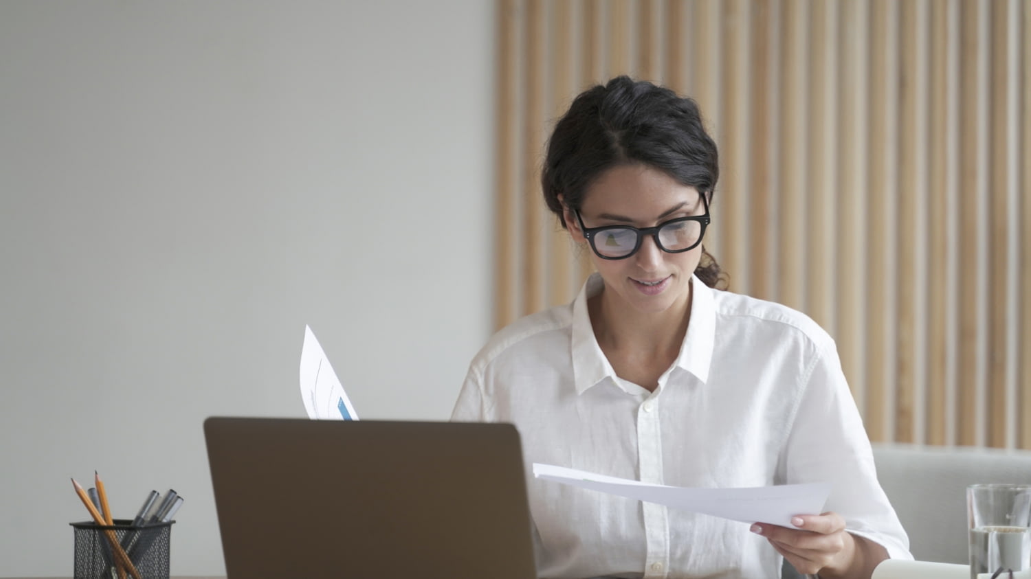 Geschäftsfrau sitzt mit Laptop und Papieren am Schreibtisch