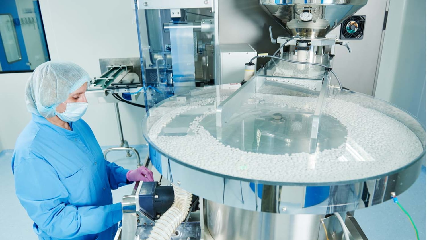 Eine Mitarbeiterin in einem pharmazeutischen Betrieb überwacht die maschinelle Herstellung von Tabletten