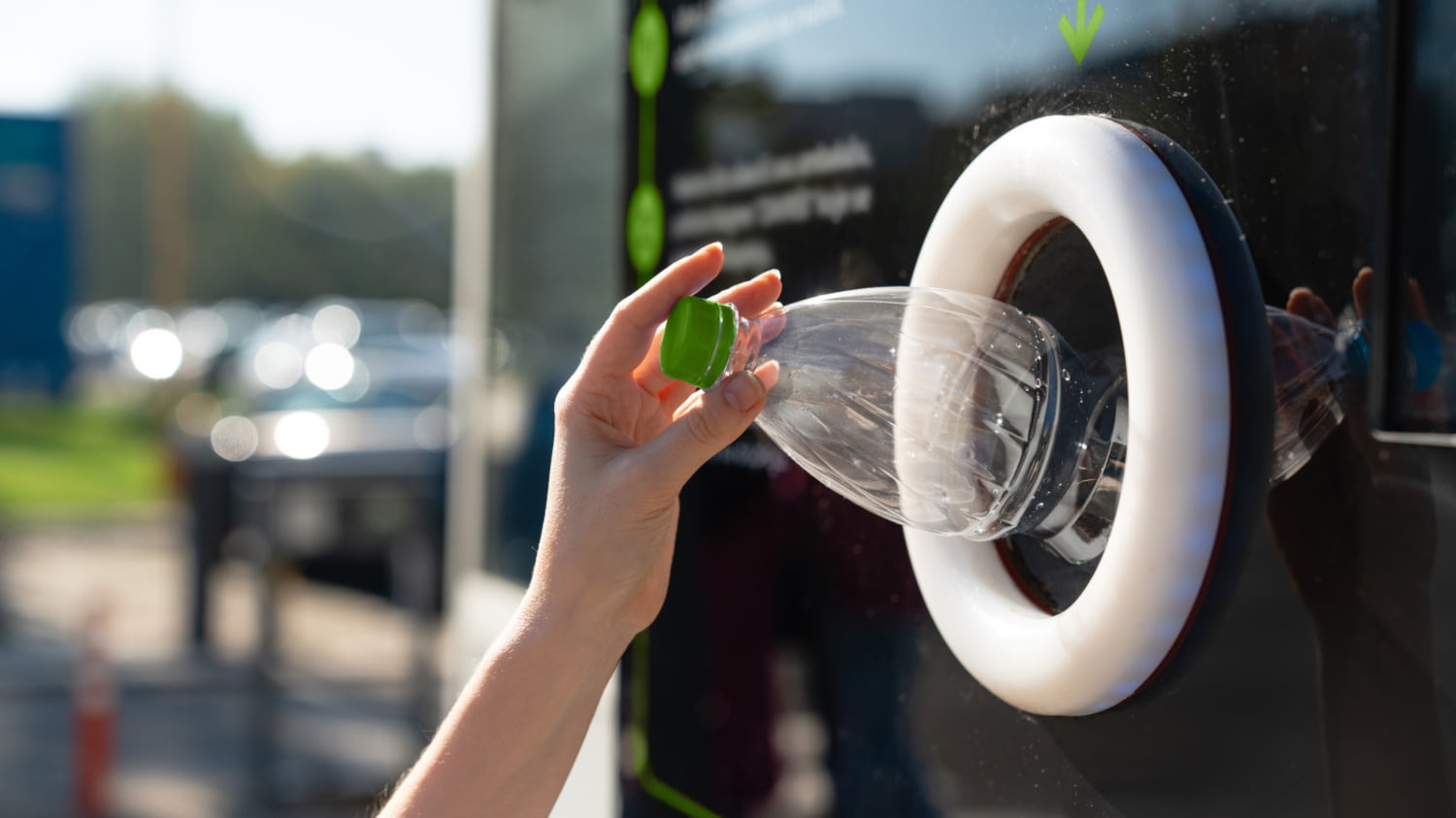 Die Hand einer Frau steckt eine leere Flasche in einen Pfandautomaten
