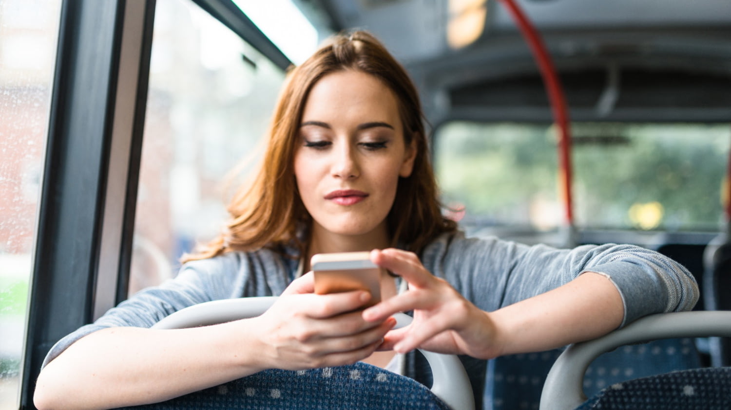 Eine junge Frau sitzt im Bus und sieht nachdenklich auf ihr Handy.