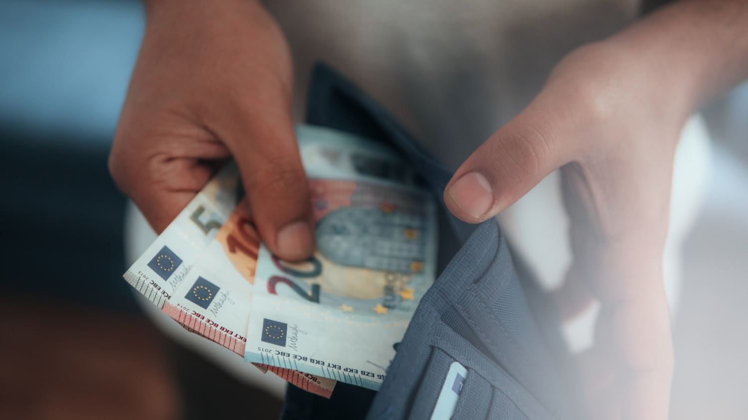 Jemand steckt mehrere Euro-Scheine in eine Geldbörse