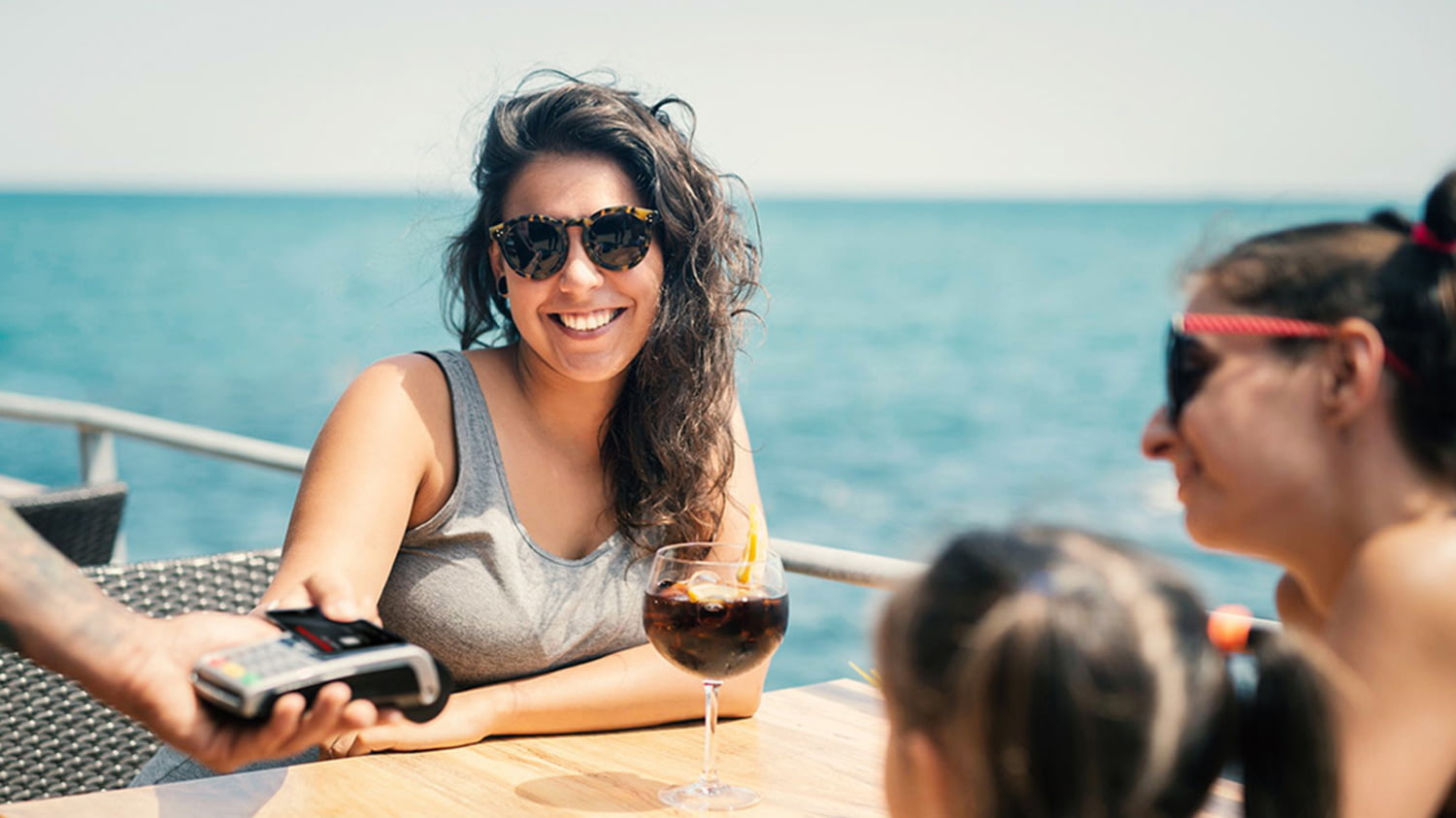 Junge Frau zahlt per Karte einen Cocktail in einer Strandbar
